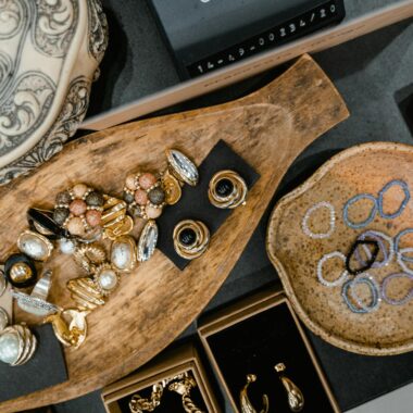 A top view of assorted jewelry including rings and bracelets in a wooden tray and ceramic dish.