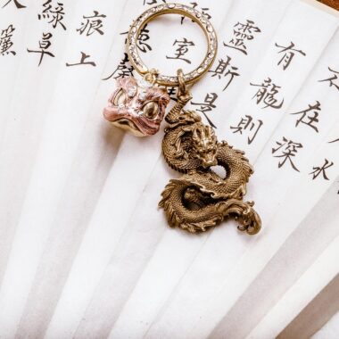 Close-up of a golden dragon pendant on a decorative fan with Asian script.